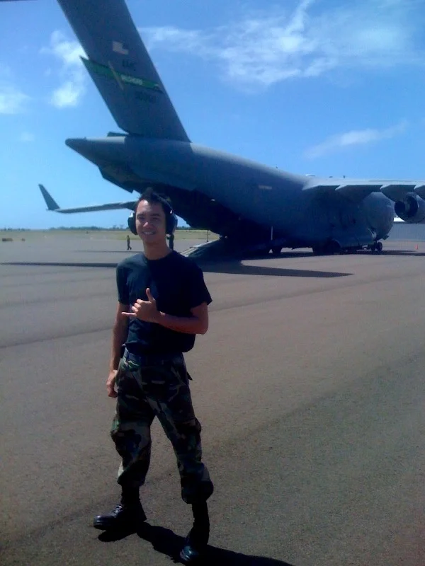 Andre making a shaka gesture beside a military cargo aircraft