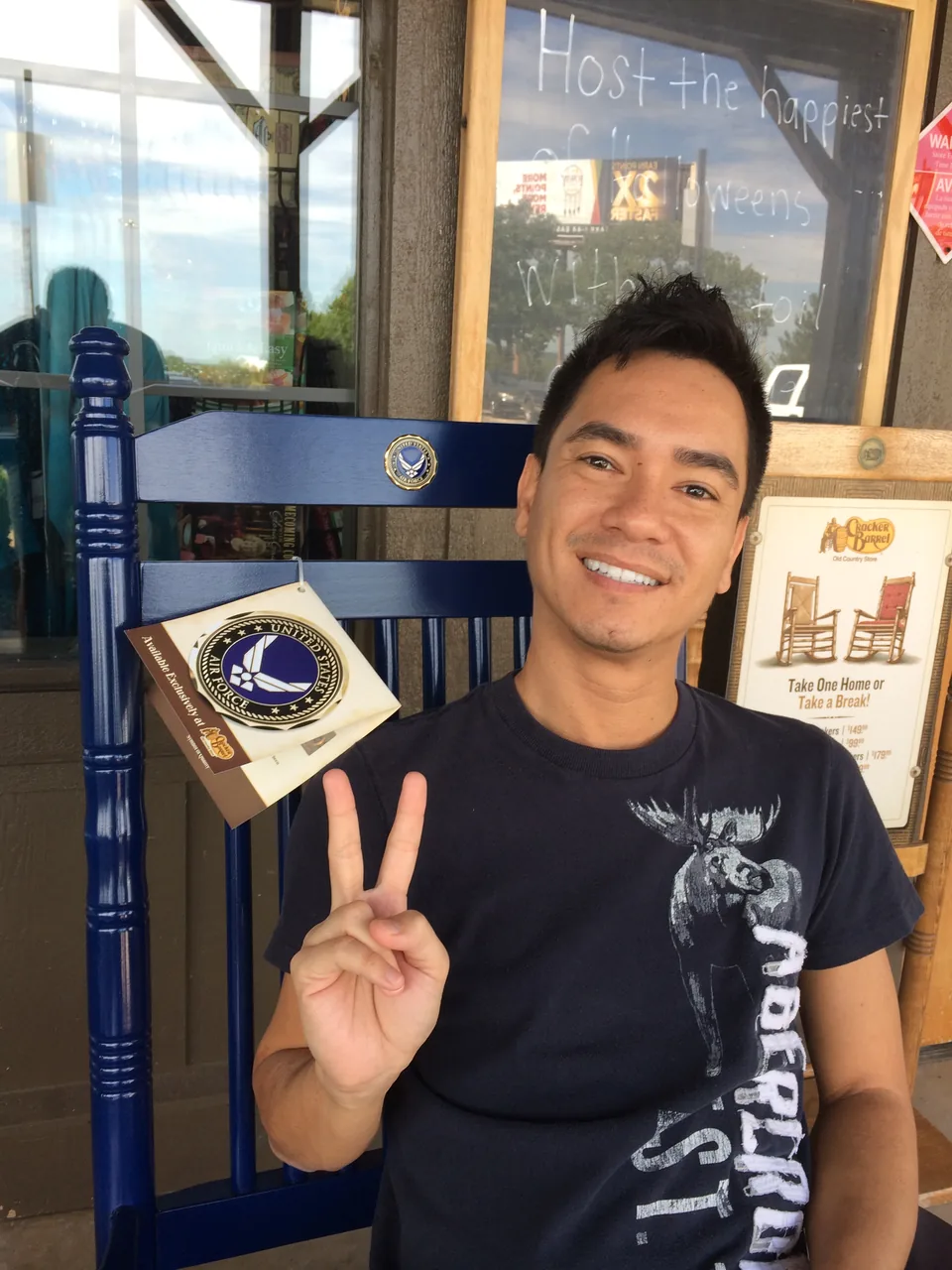 Andre smiling and holding up a peace sign while seated in a blue rocking chair.